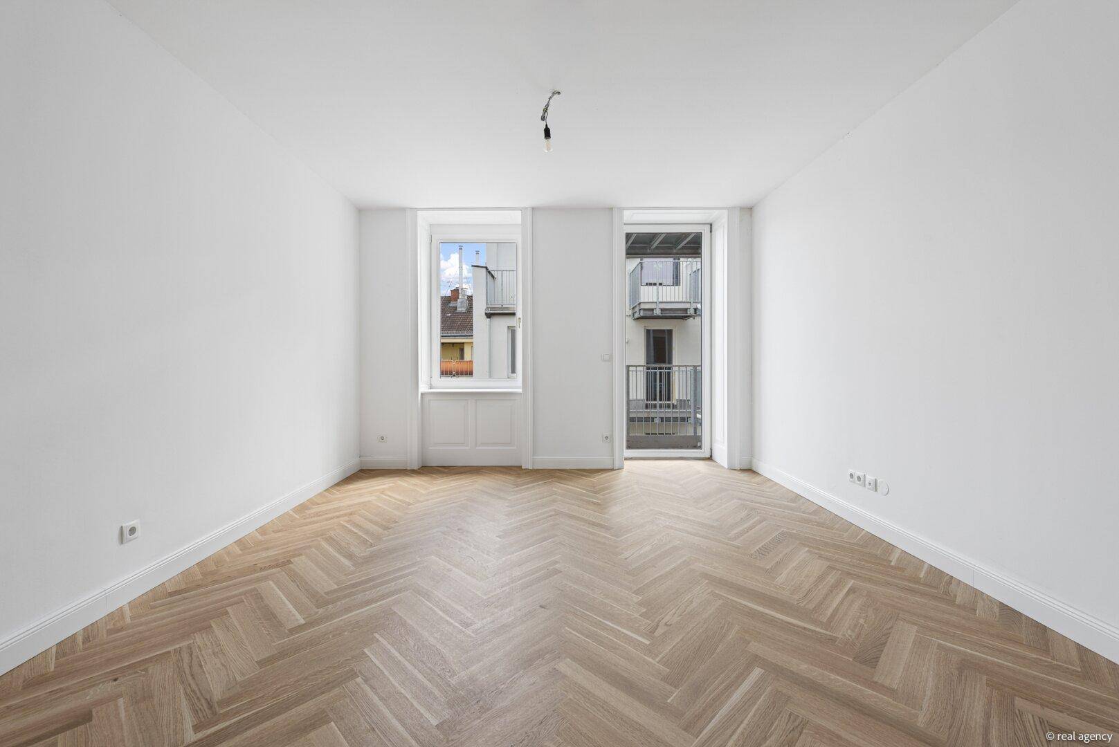 Großer, heller Raum mit Fischgrätparkettboden und direktem Zugang zum Balkon.