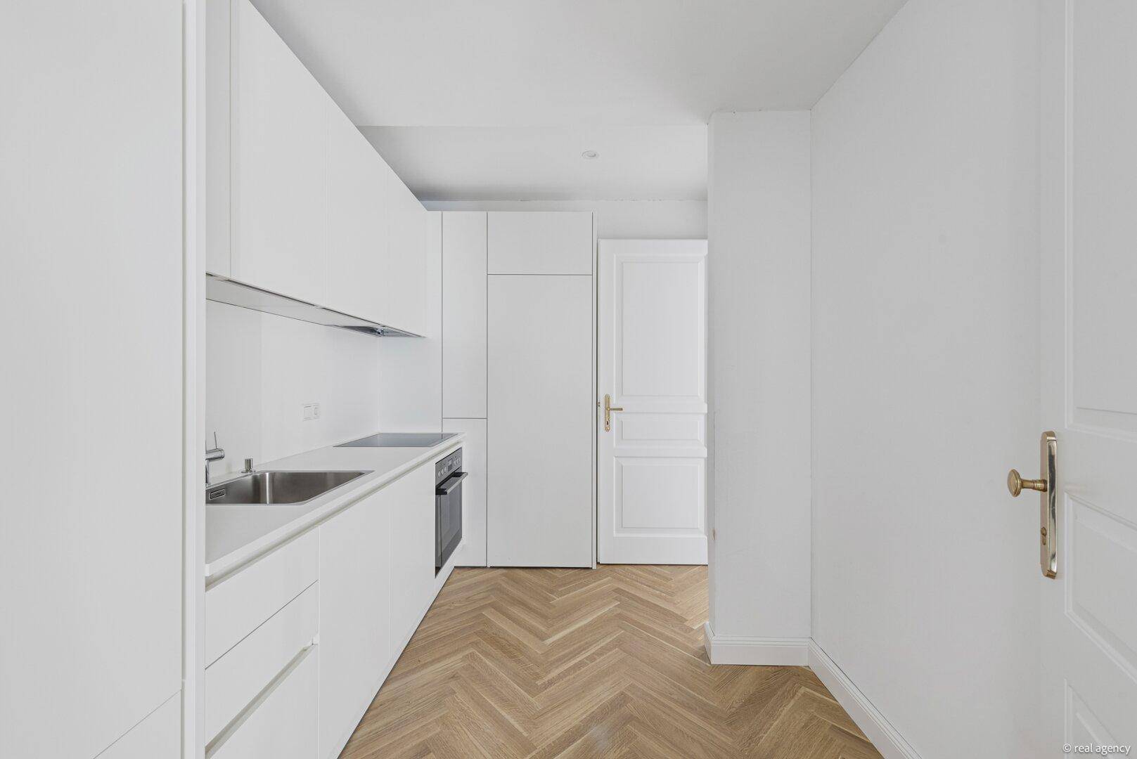 Moderne, weiße Einbauküche mit integrierten Geräten und elegantem Fischgrätparkettboden.