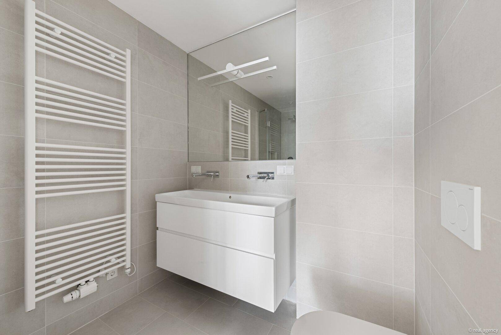 Modernes Badezimmer mit grauen Fliesen, schwebendem Waschtisch und beheiztem Handtuchhalter.