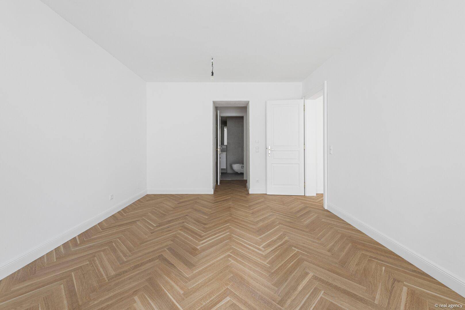 Heller Eingangsbereich mit Fischgrätparkett und Zugang zu weiteren Räumen, inklusive Badezimmer.