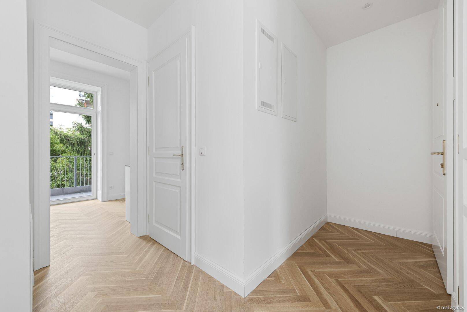Heller Flur mit Fischgrätparkett und Zugang zu einem französischen Balkon.