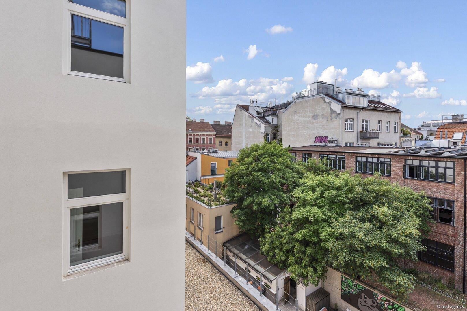 Blick über die Dächer der Stadt mit viel Grün und blauem Himmel.