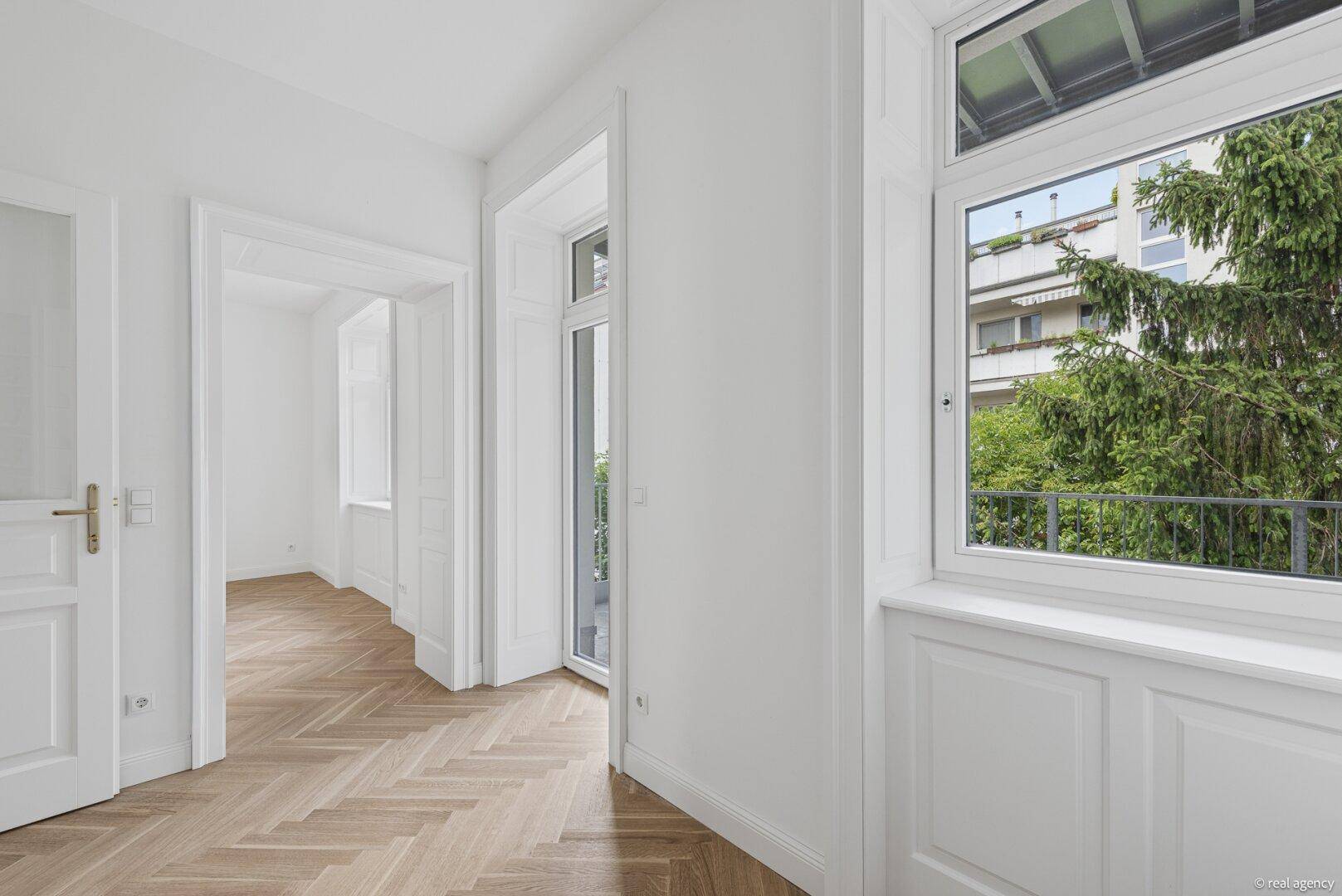 Helles Zimmer mit Fischgrätparkett und Zugang zu einem französischen Balkon.