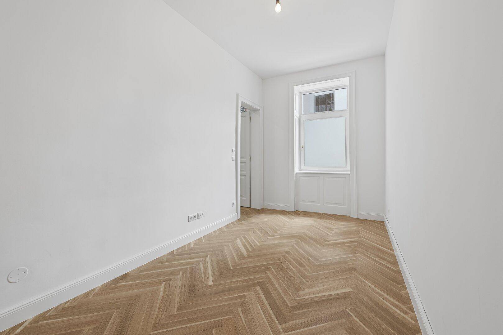 Kleiner, heller Raum mit Fischgrätparkett und einem Fenster, ideal als Schlaf- oder Arbeitszimmer.