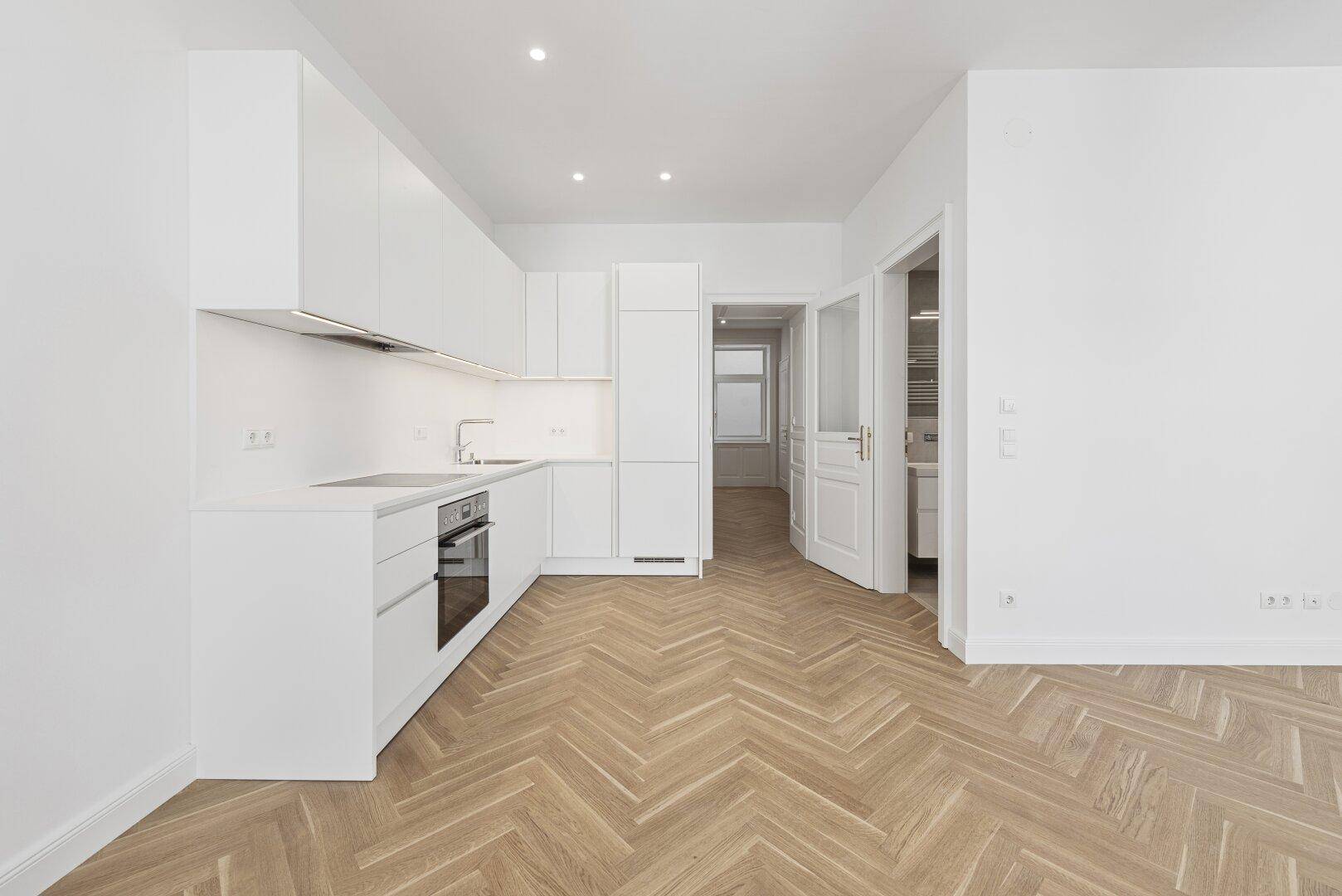 Moderne, helle Küche mit weißen Schränken, integrierten Geräten und Fischgrätparkettboden.