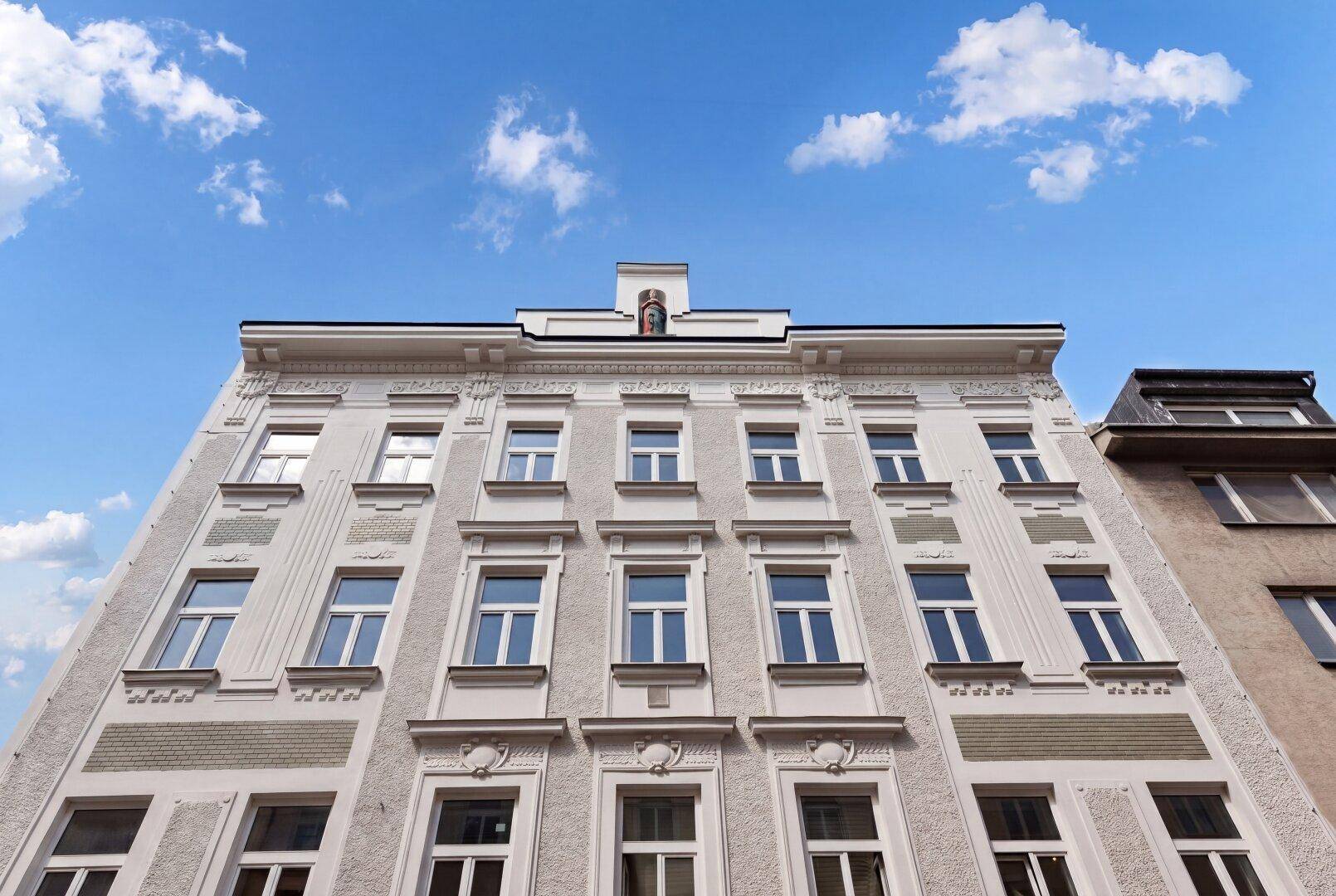 Fassade eines eleganten Altbaus mit zahlreichen Fenstern und dekorativen Stuckelementen unter blauem Himmel.