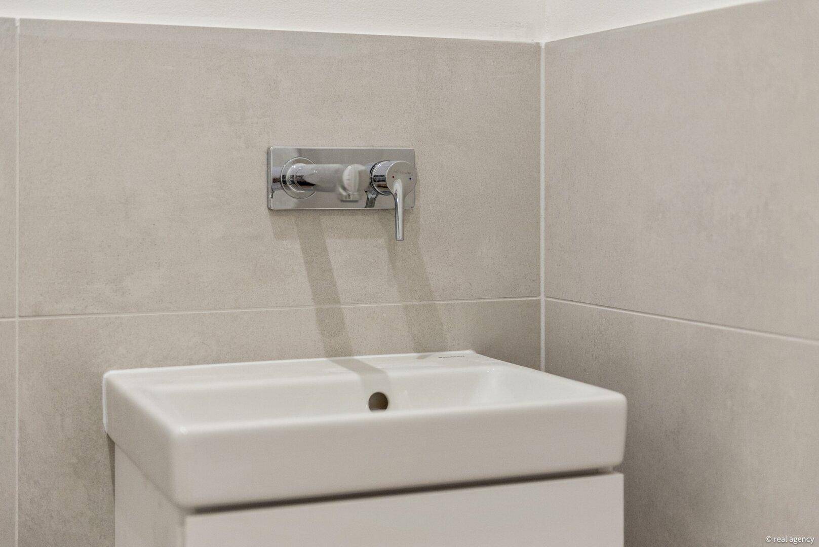 Modernes Waschbecken mit elegantem Wandhahn und hellen Fliesen im Badezimmer.
