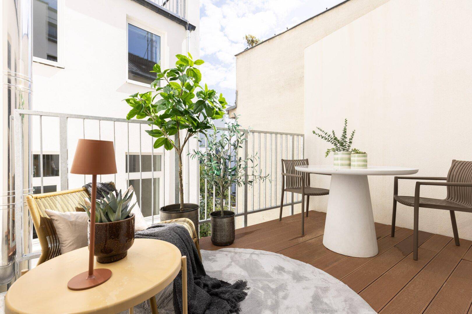 Möblierter Balkon mit Holzboden, Pflanzen und Sitzgelegenheiten für entspannte Stunden.