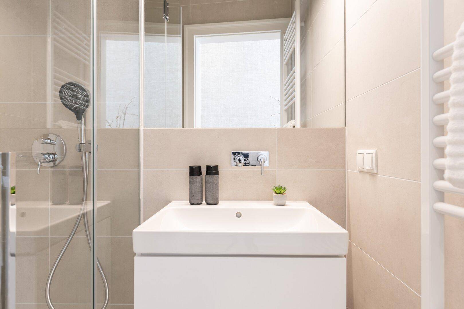 Modernes Badezimmer mit Waschtisch, Spiegel, Duschkabine und beheiztem Handtuchhalter.
