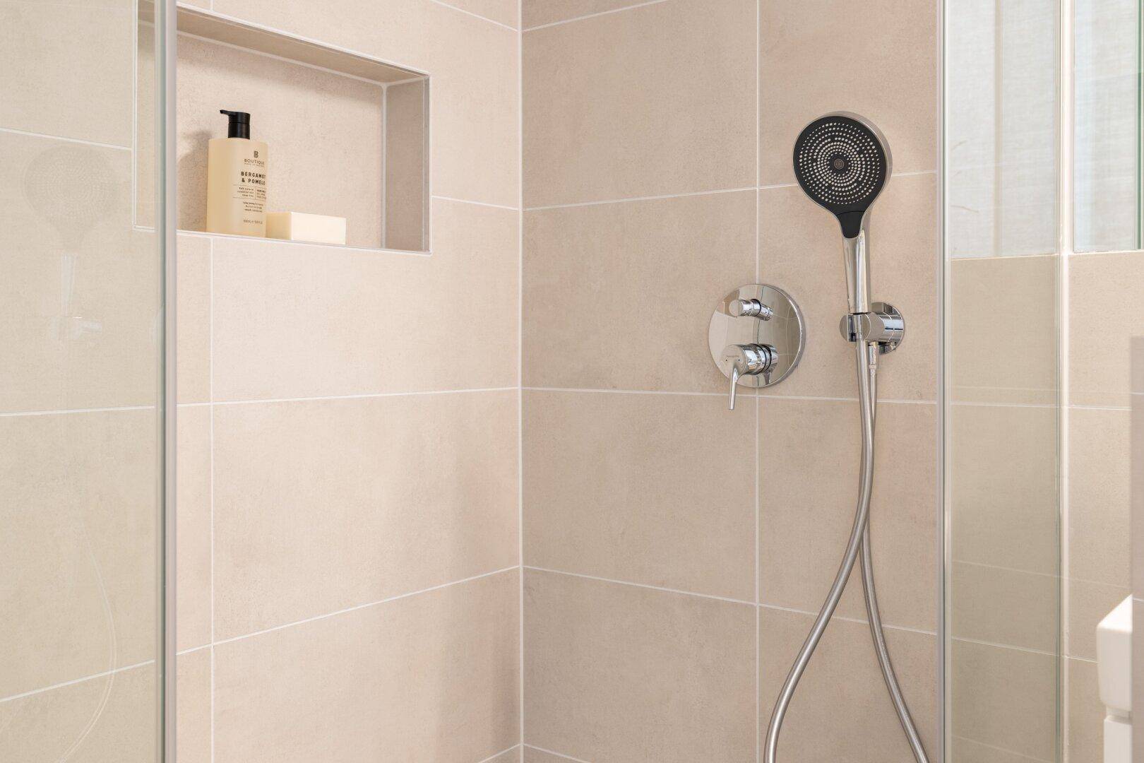 Nahaufnahme einer modernen begehbaren Dusche mit beigefarbenen Fliesen und Duschkopf.