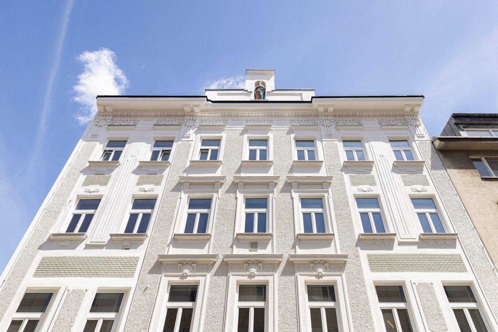 Historische Fassade eines Altbaus mit reich verzierten Details und vielen Fenstern.