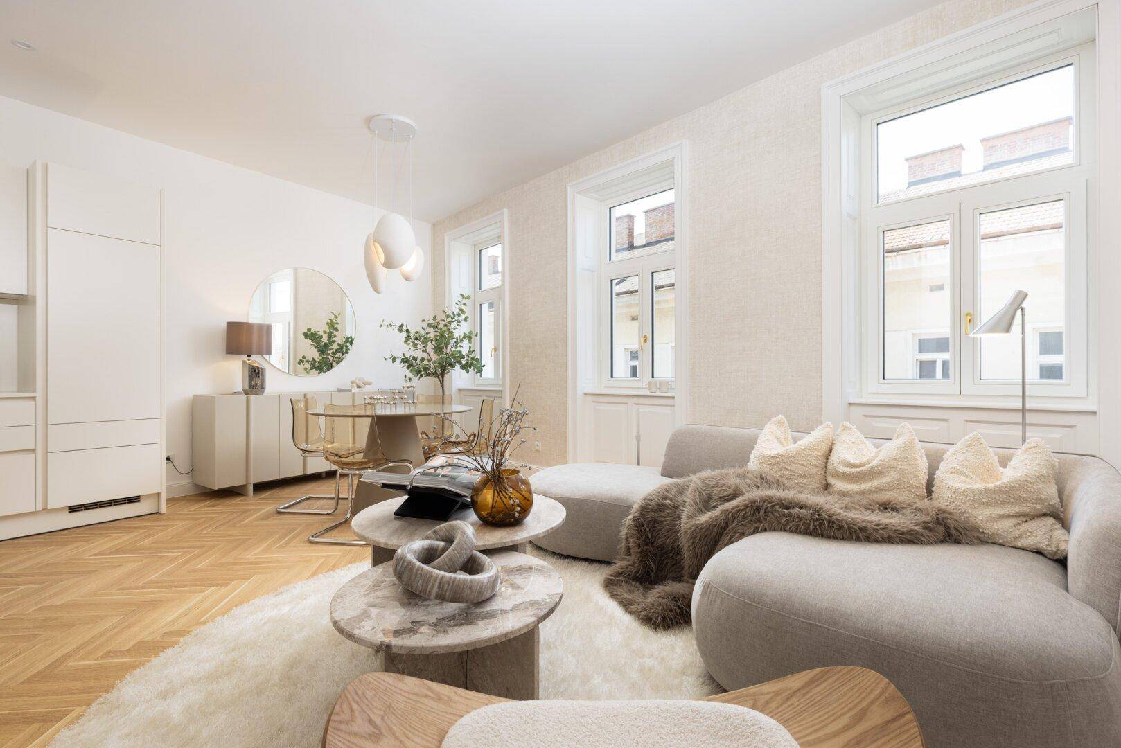 Gemütlicher Wohn- und Essbereich mit modernem Sofa, runden Tischen und Fischgrätparkett.