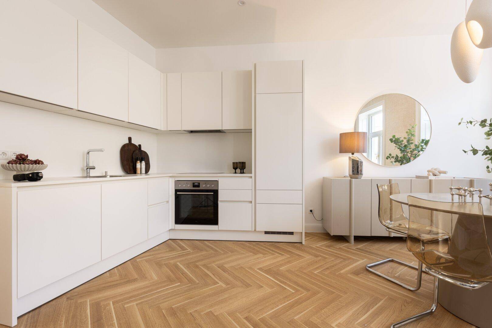 Moderne weiße Einbauküche mit integriertem Backofen, Spüle und Fischgrätparkett.