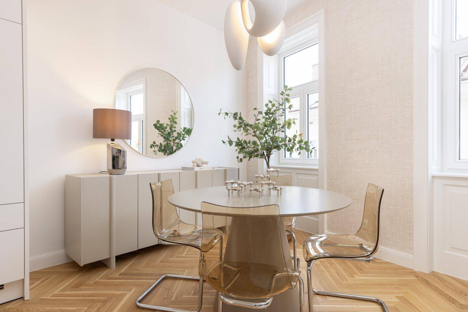 Eleganter Essbereich mit rundem Tisch, transparenten Stühlen und einem großen Wandspiegel.