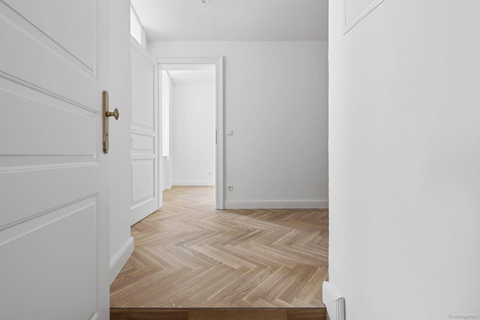 Heller Flur mit elegantem Fischgrätparkettboden und Zugang zu weiteren Räumen.
