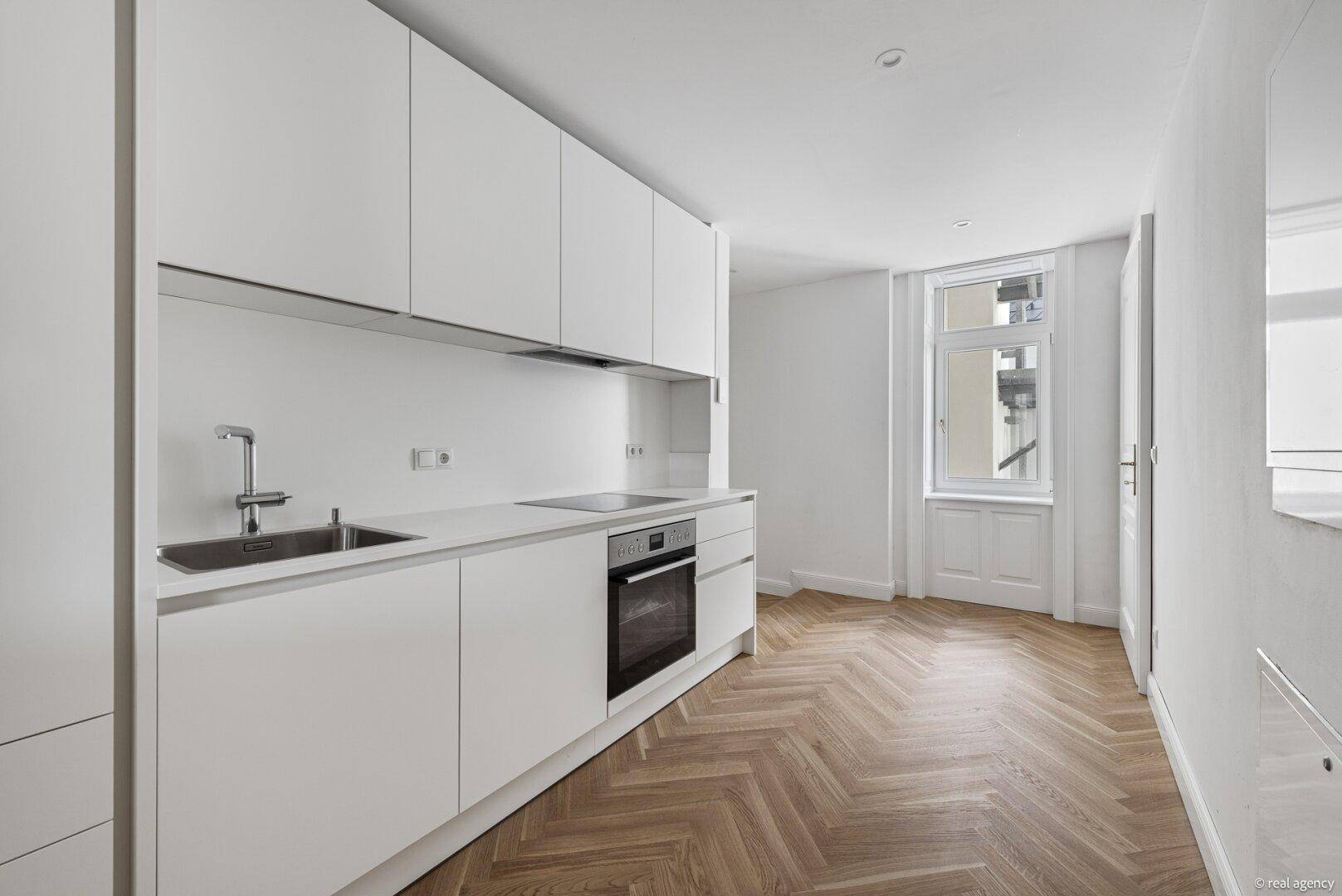 Stilvolle, helle Küche mit minimalistischen weißen Fronten und elegantem Fischgrätparkettboden.