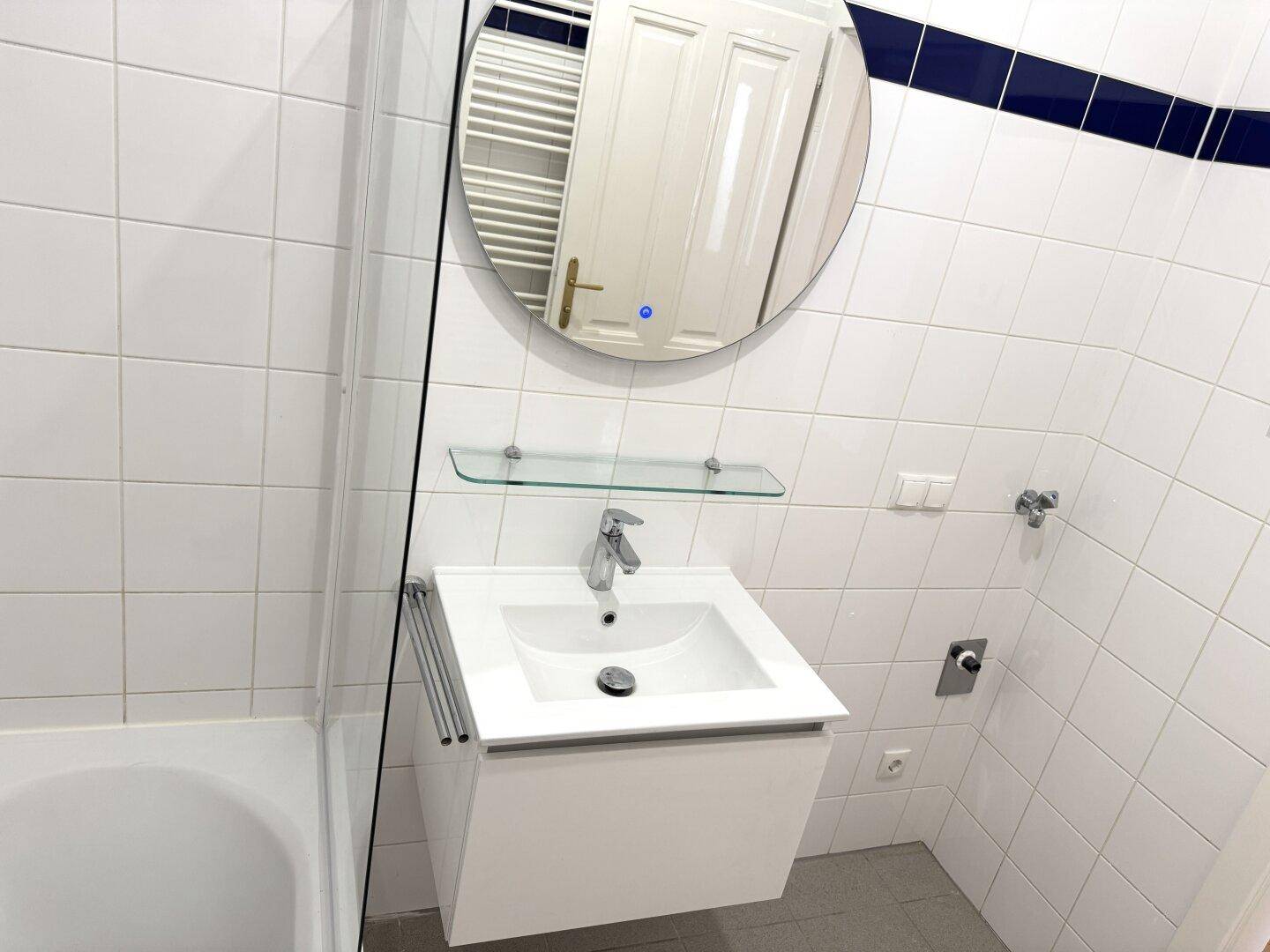Detailansicht des modernen Badezimmers mit Waschbecken, rundem Spiegel und beheiztem Handtuchhalter.