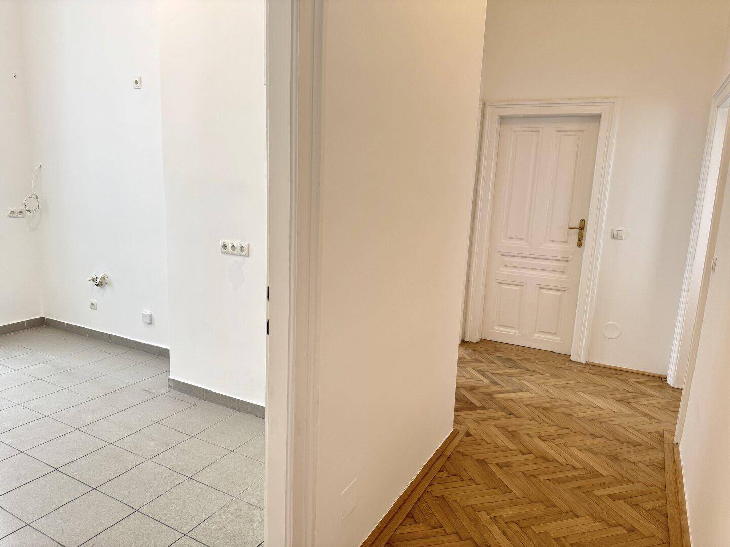 Übergangsbereich mit Fischgrätparkett und Fliesenboden, der verschiedene Bereiche der Wohnung verbindet.