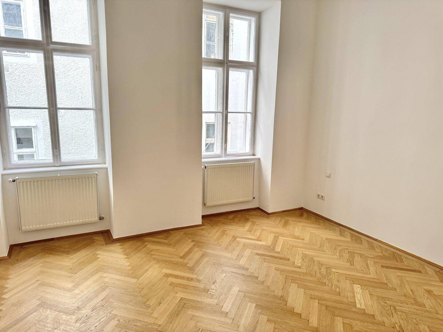 Helles Zimmer mit Fischgrätparkett und zwei Fenstern, das sich gut als Schlaf- oder Kinderzimmer eignet.
