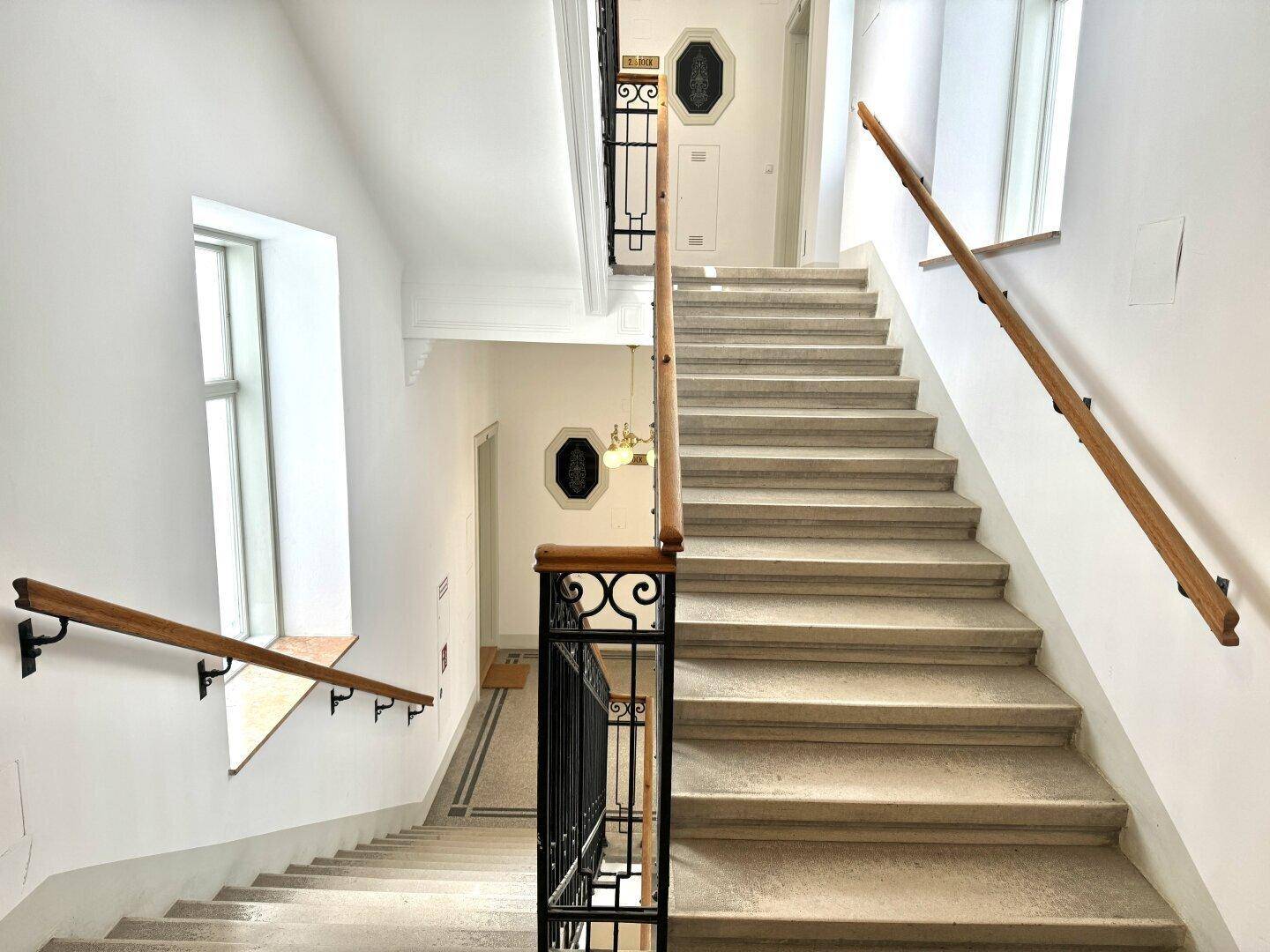 Elegantes Treppenhaus mit Holzhandläufen und großen Fenstern, die viel Licht hereinlassen.