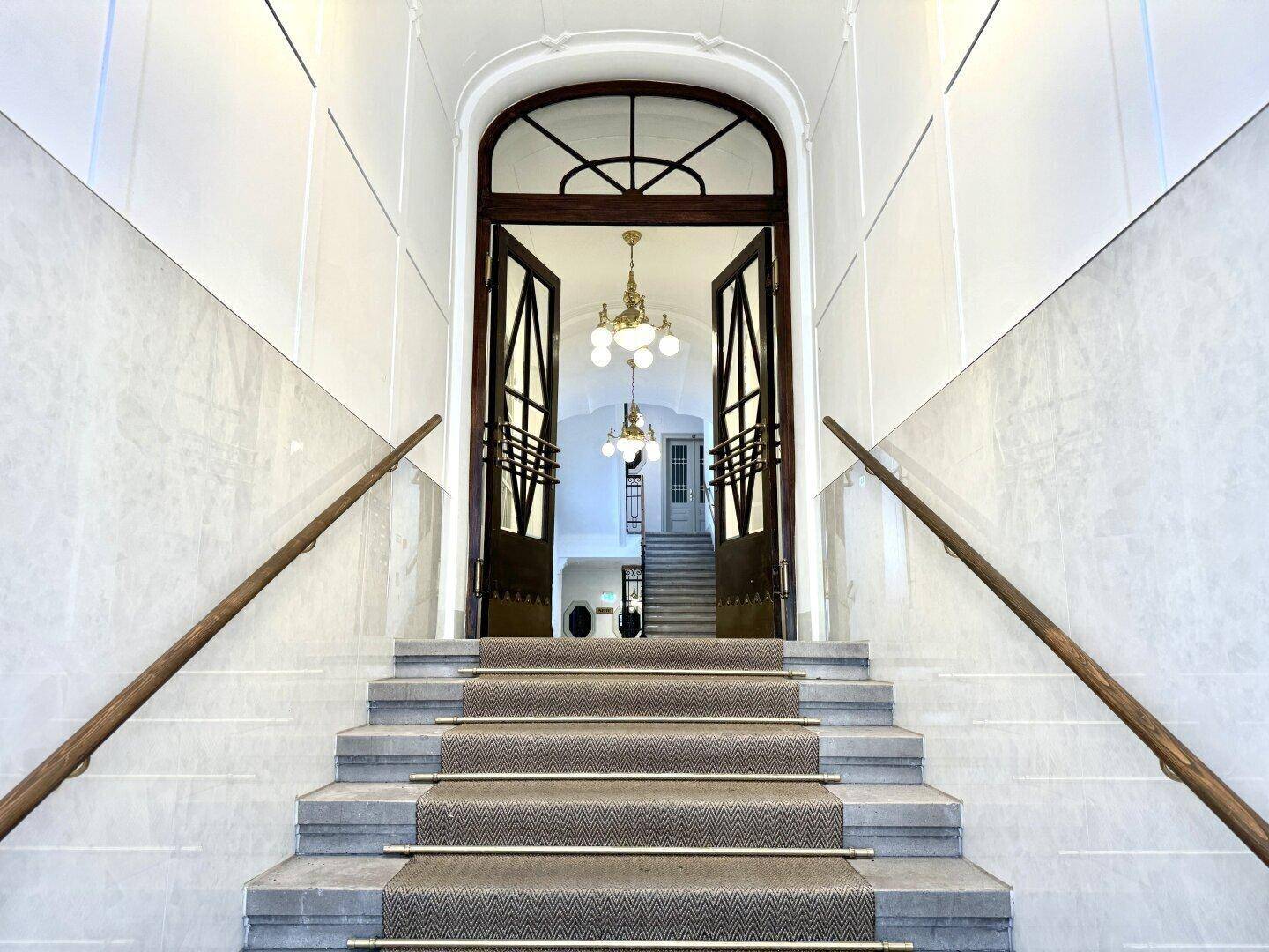 Repräsentativer Eingangsbereich mit Marmortreppe, eleganten Türen und Kronleuchtern, der zum Obergeschoss führt.
