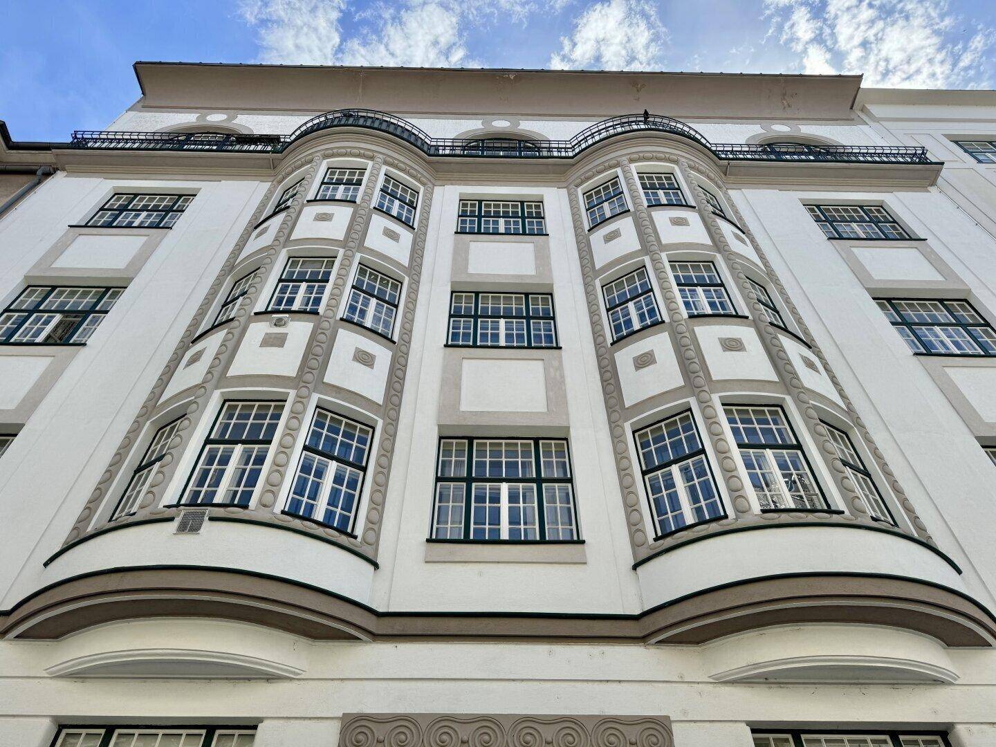 Historische Fassade eines Altbaus mit markanten Erkerfenstern und dekorativen Elementen unter blauem Himmel.