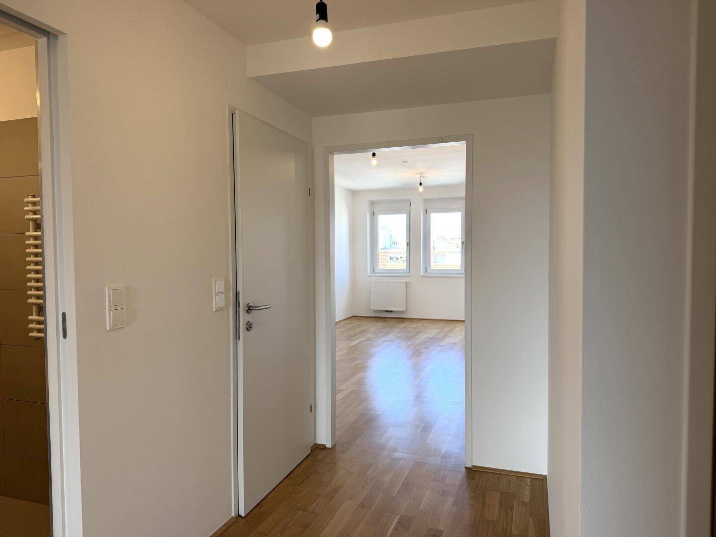 Heller Flur mit Holzboden, der zu einem weiteren Zimmer und dem Badezimmer führt.