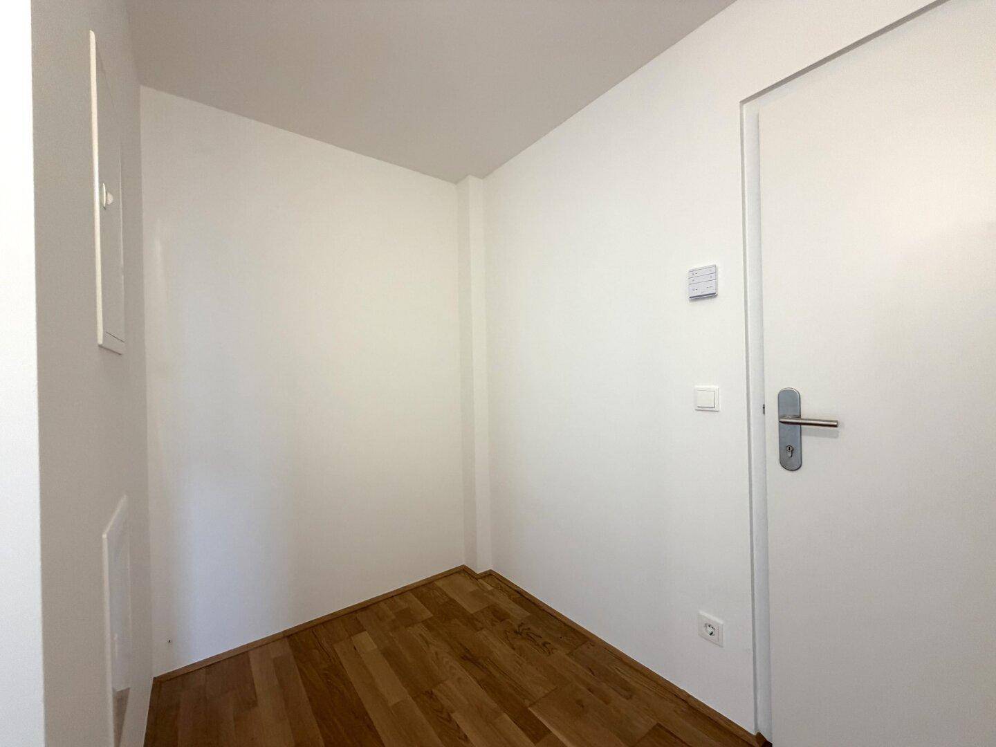 Heller, leerer Eingangsbereich mit Holzboden und weißen Wänden.