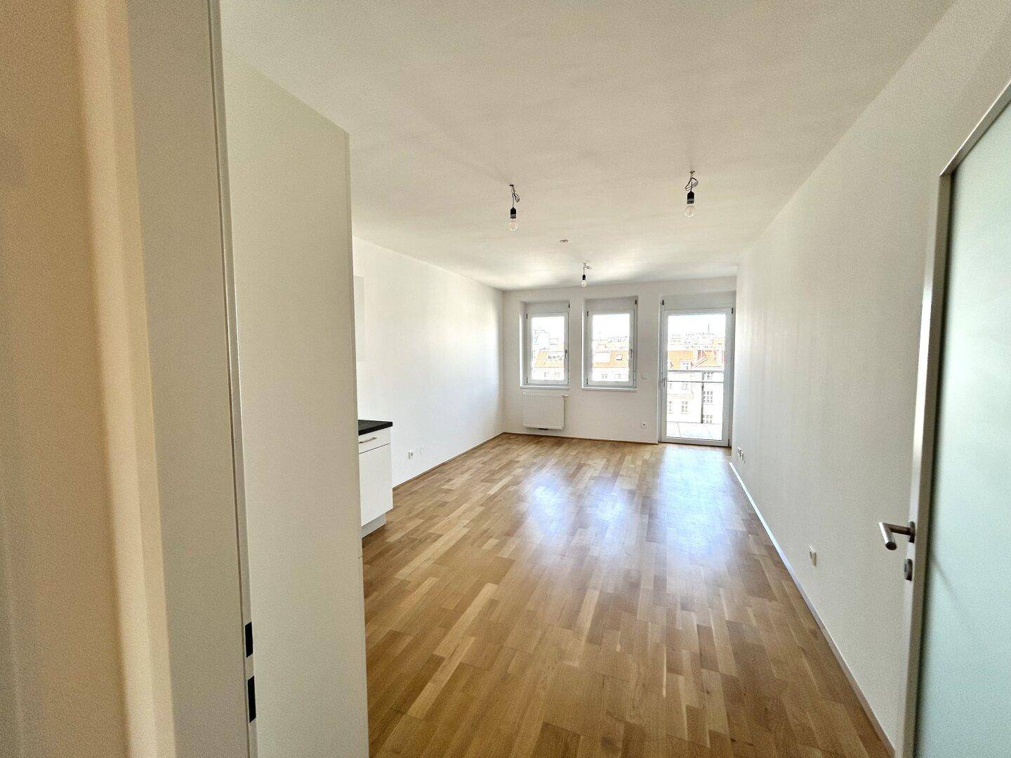 Geräumiges Wohnzimmer mit Holzboden, großen Fenstern und Zugang zum Balkon.