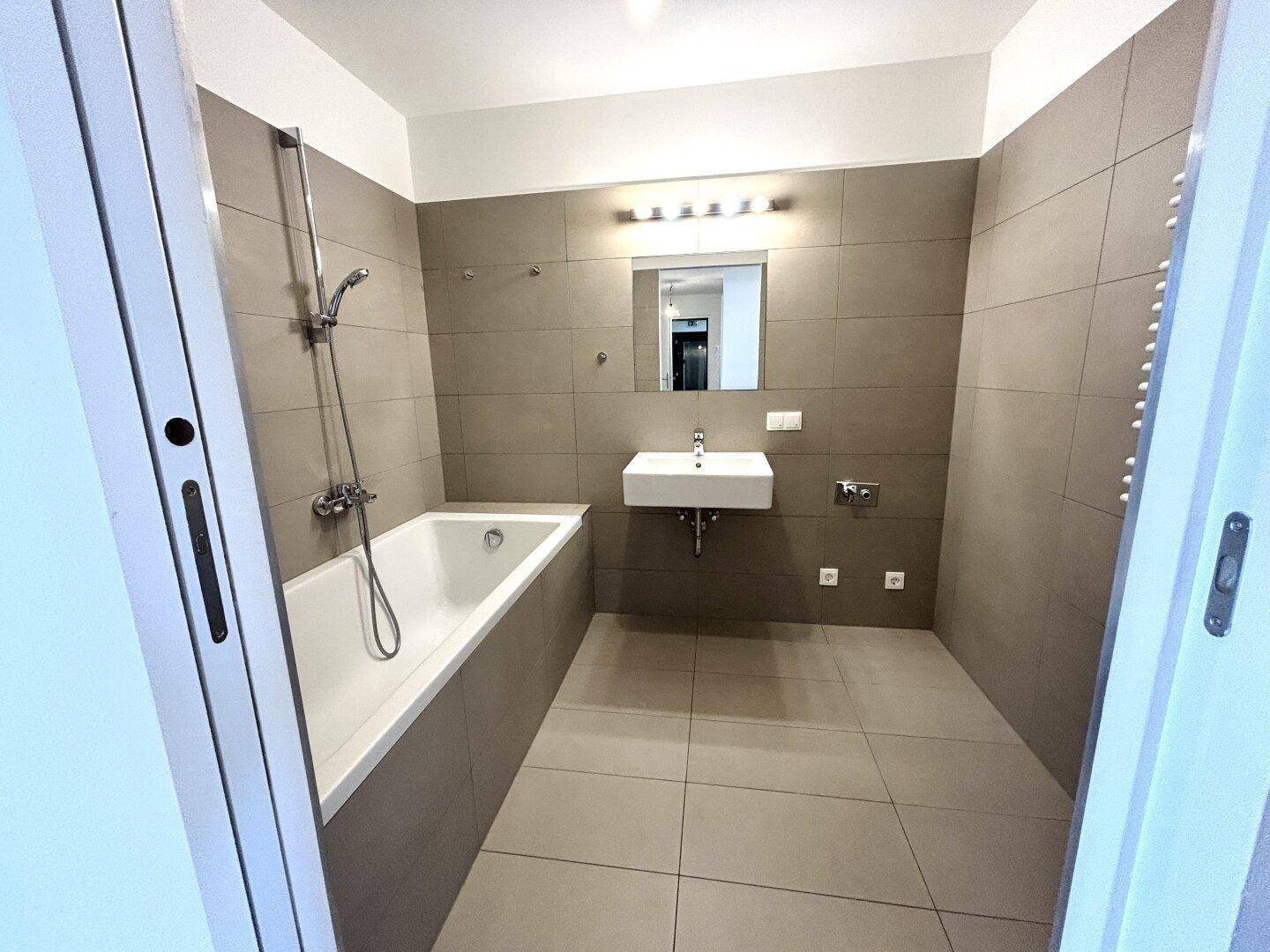 Modernes Badezimmer mit Badewanne, Waschbecken und grauen Fliesen.