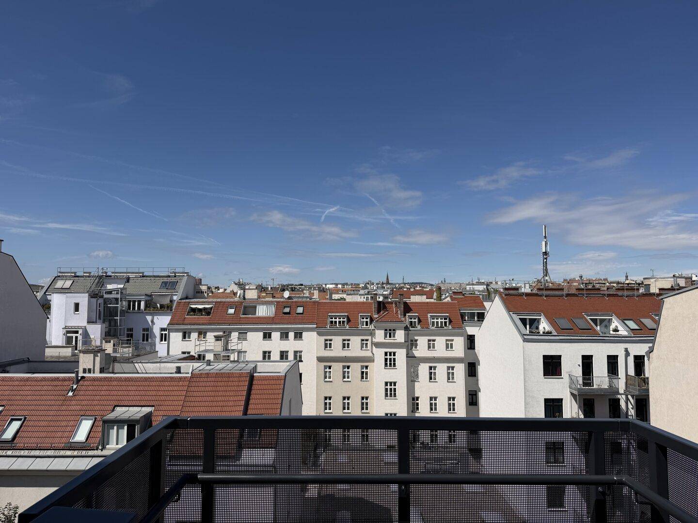 Balkon mit weitem Blick über die Dächer der Stadt unter blauem Himmel.