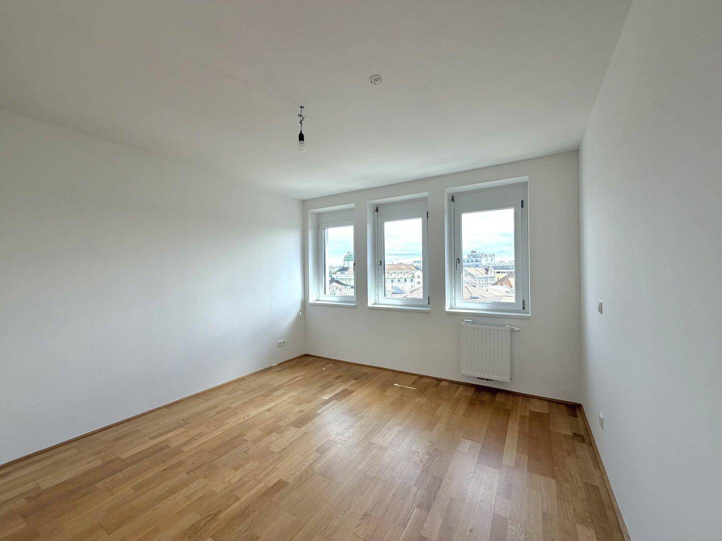 Helles Schlafzimmer mit Holzboden und drei Fenstern mit Stadtblick.