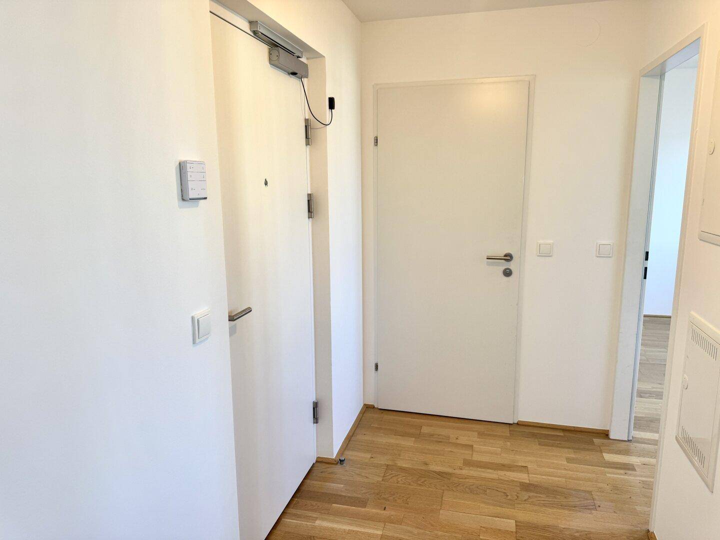 Heller Eingangsbereich mit Holzboden und zwei weißen Türen, die zu den Zimmern führen.