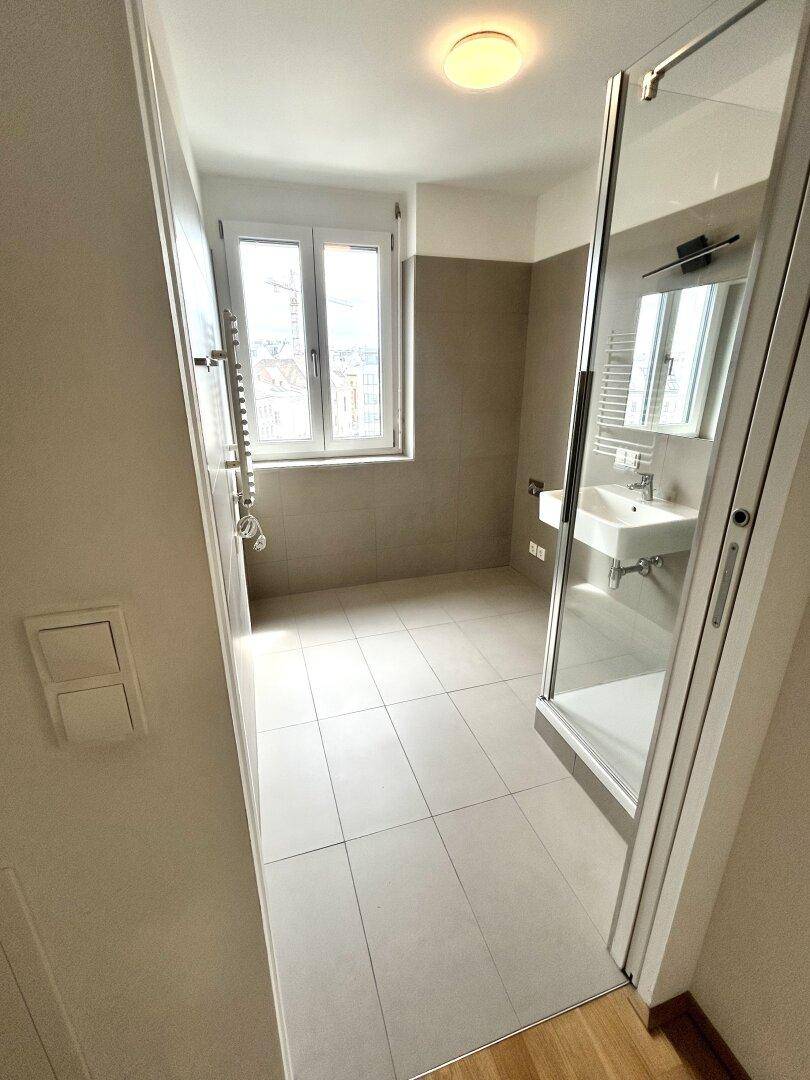 Modernes Badezimmer mit Duschkabine, Waschbecken, Fenster und hellen Fliesen.