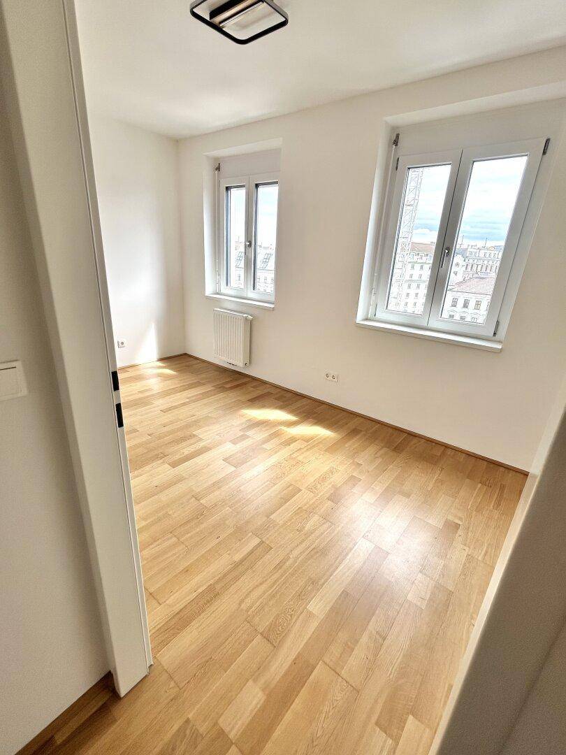 Helles Zimmer mit zwei Fenstern, Holzboden und viel natürlichem Licht.
