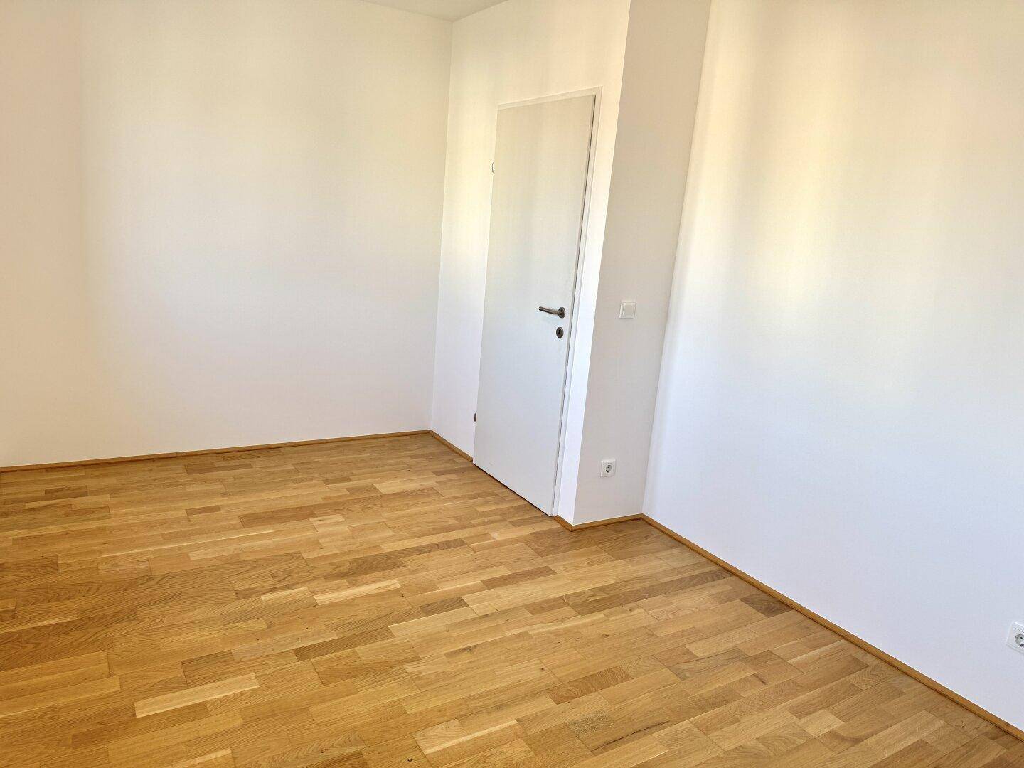 Leeres Zimmer mit hellem Holzboden und weißen Wänden, bereit zur individuellen Gestaltung.