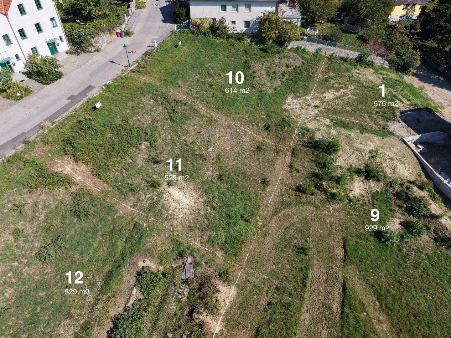 Luftaufnahme von mehreren Baugrundstücken mit Flächenangaben in ländlicher Umgebung und angrenzender Straße.