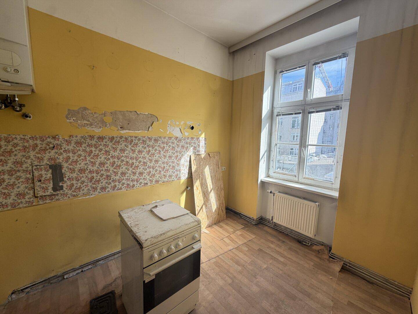 Küche in Renovierungszustand mit gelben Wänden, altem Herd und Fenster.