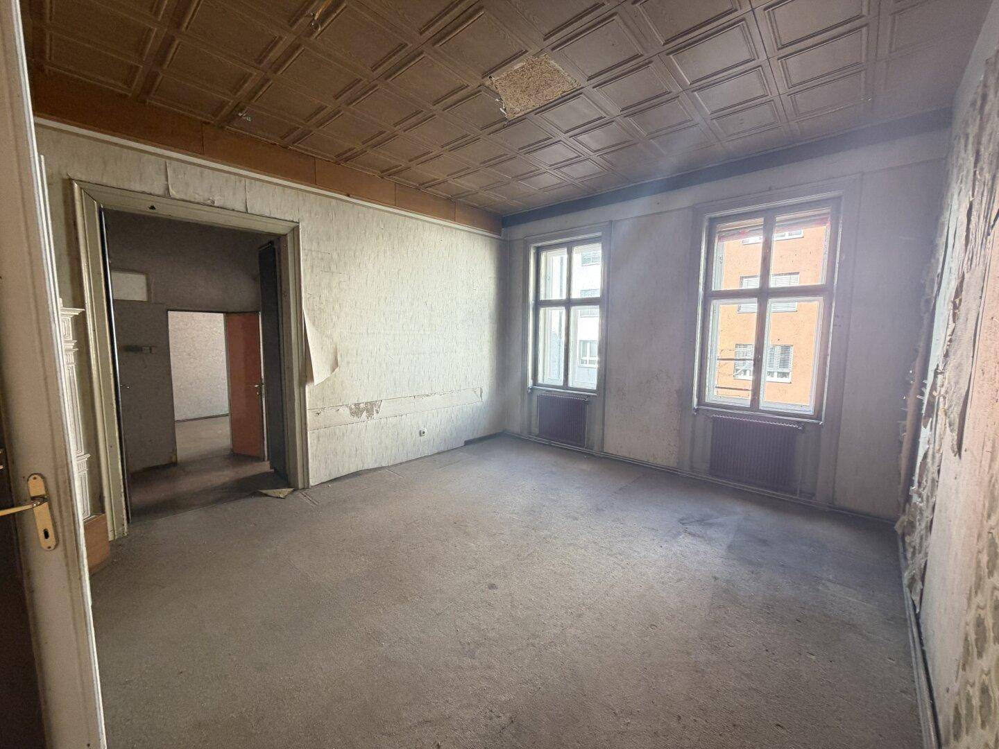 Unrenoviertes Zimmer mit alter Deckenverkleidung und abgenutztem Bodenbelag.