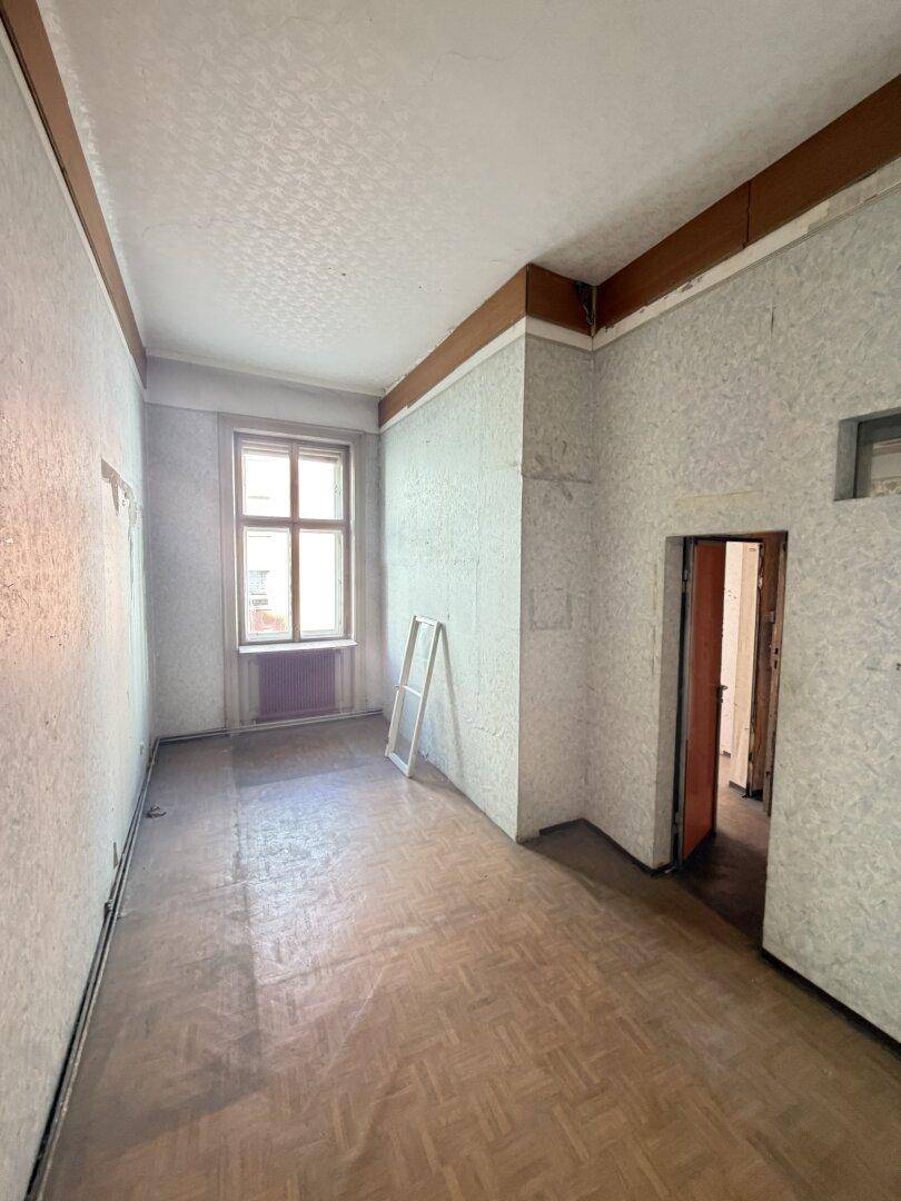Langes Zimmer mit Fischgrätparkett und Fenster, bereit für eine Renovierung.