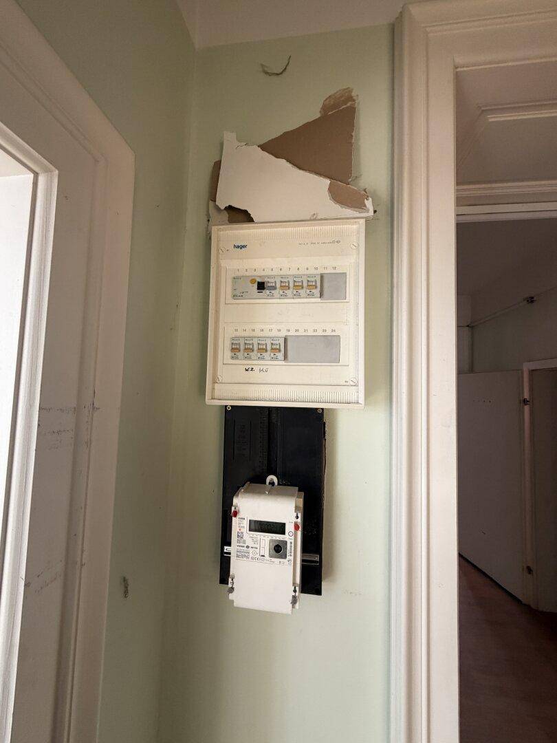 Elektrischer Sicherungskasten an einer hellgrünen Wand in einem Flur.