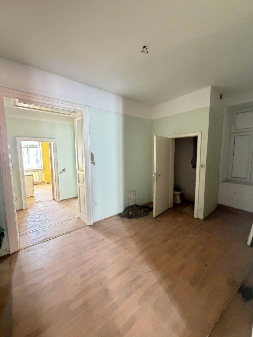 Geräumiges Zimmer mit Holzboden und Zugang zu einem kleinen WC.