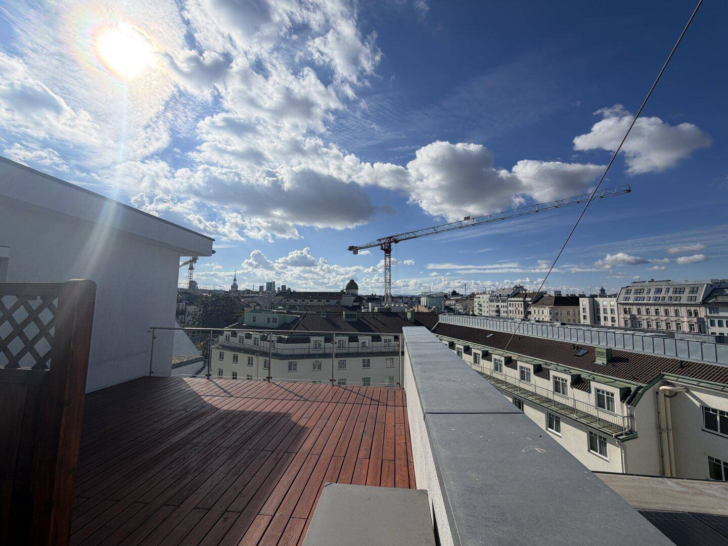 Sonniger Dachterrassenbereich mit Holzdeck und Glasgeländer, bietet einen beeindruckenden Stadtblick.