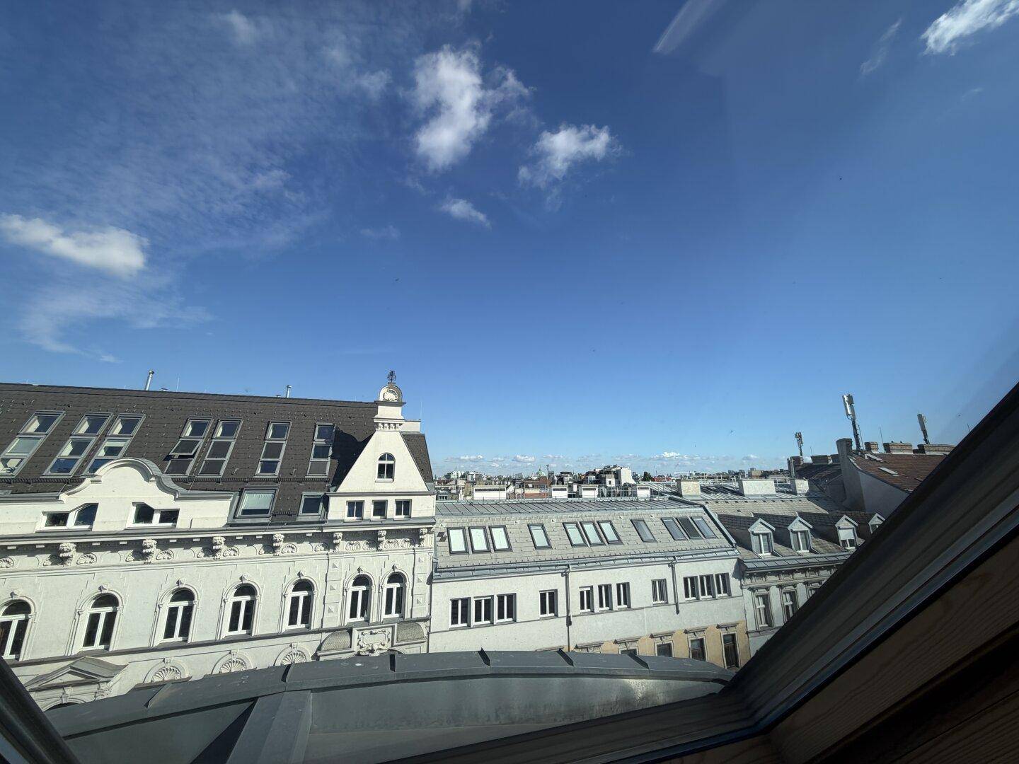 Panoramablick aus dem Fenster über die Dächer der Stadt, mit historischer und moderner Architektur.