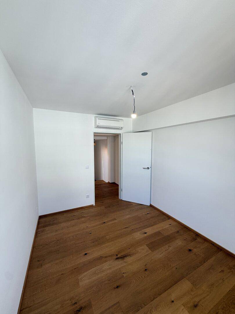 Helles Schlafzimmer mit Holzboden, weißen Wänden und Klimaanlage, bereit zur individuellen Gestaltung.