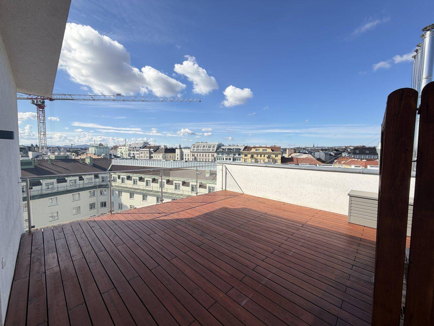 Weitläufige Dachterrasse mit Holzdeck und Glasgeländer, bietet einen Panoramablick über die Stadt.