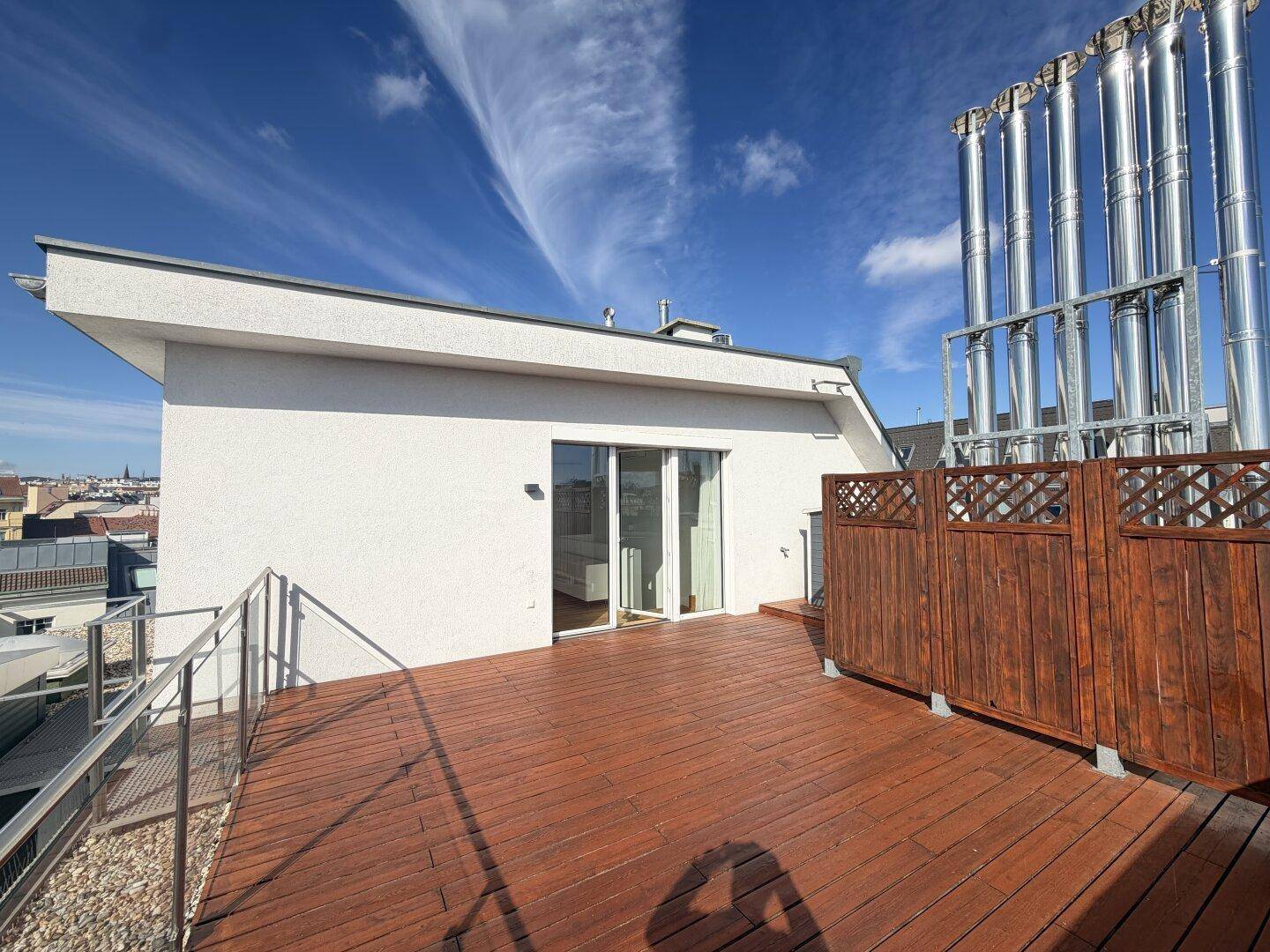 Geräumige Dachterrasse mit Holzdeck und Glasgeländer, bietet einen weiten Blick über die Dächer der Stadt.