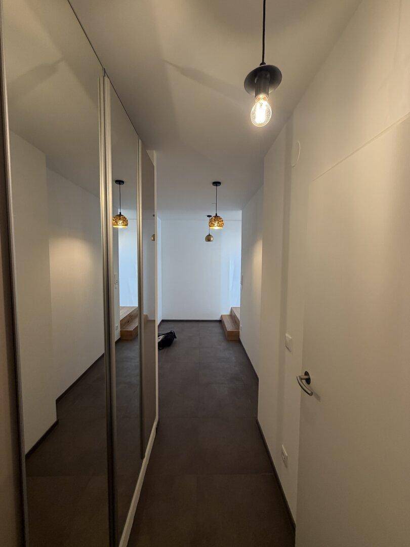 Heller Flur mit dunklem Boden und integrierten Spiegelschränken, die den Raum optisch vergrößern.