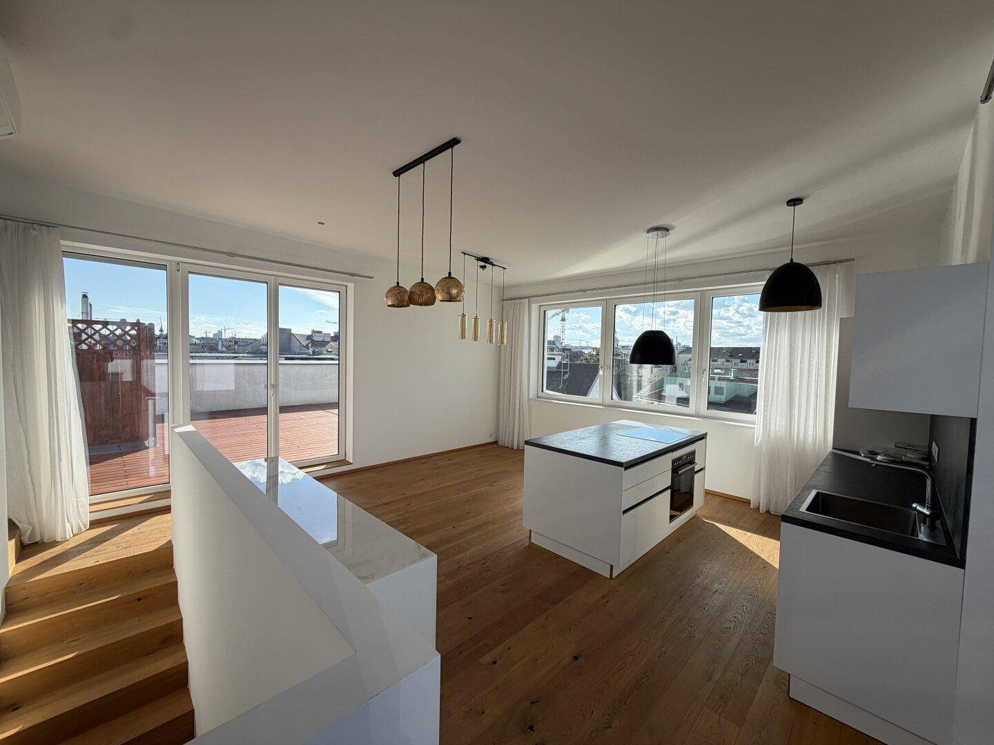 Lichtdurchfluteter Wohnbereich mit offener Küche, Holzboden und direktem Zugang zu einer sonnigen Terrasse.