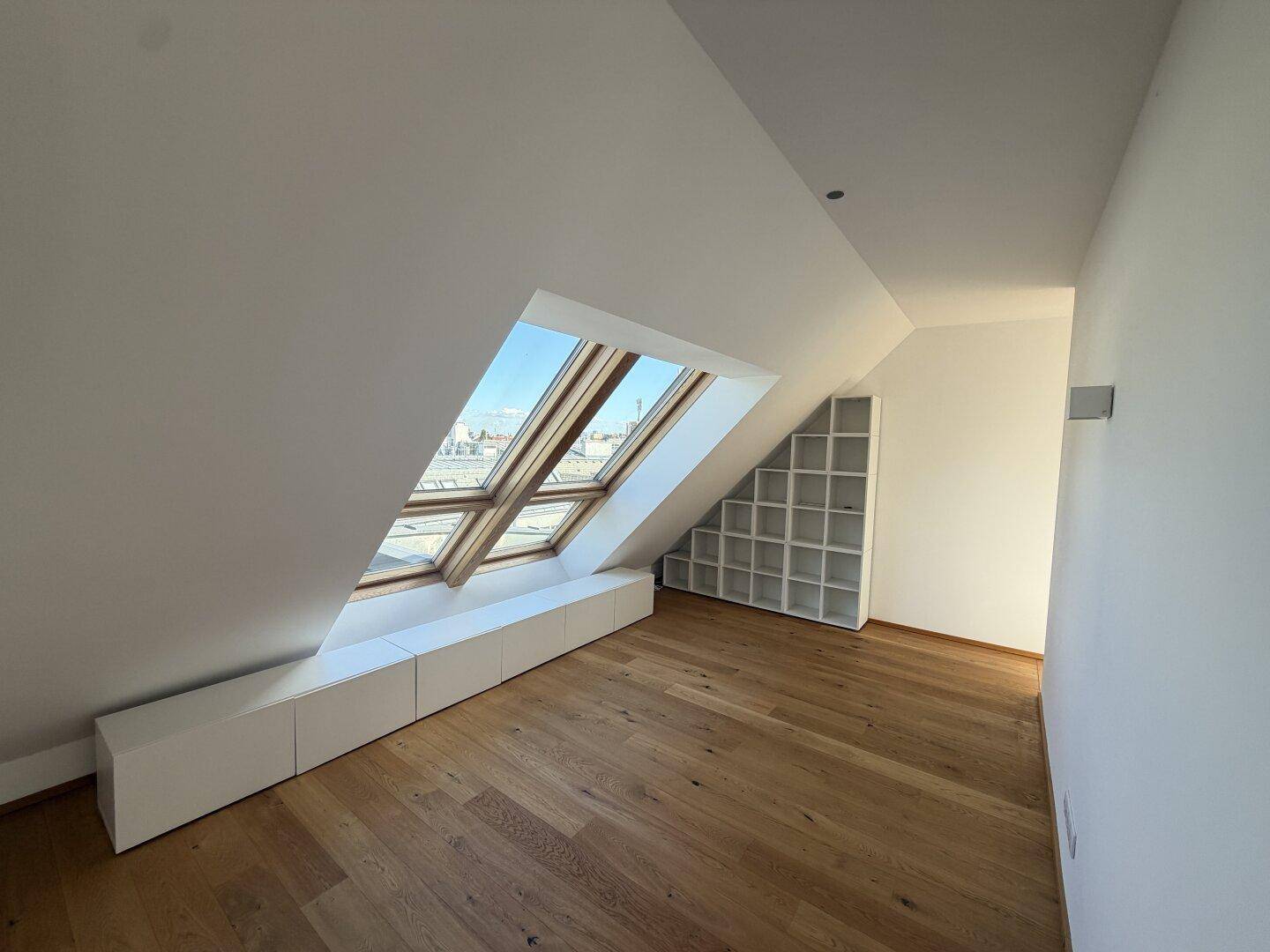 Helles Dachzimmer mit schrägen Wänden, großen Dachfenstern und integrierten Regalen, ideal als Arbeits- oder Schlafzimmer.